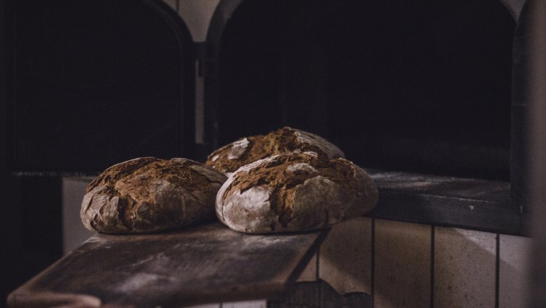 understand bread., © Bäckerei Dorfstetter Three loaves of bread on a wooden slider in front of an oven.