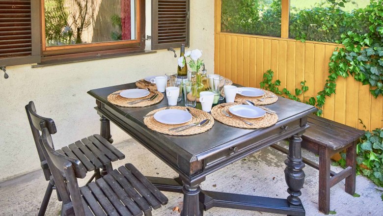 Top 1 - Terrasse, © VP FeWo OG Gedeckter Tisch auf einer Terrasse mit vier Plätzen, Holzmöbeln und Pflanzen im Hintergrund.