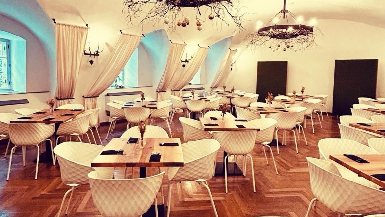 Hall of Arms in the Freiherr, © Markus Jokesz Elegant dining room with parquet floor, white chairs, wooden tables and decorative chandeliers.