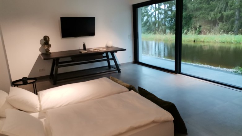 Walddenke, Schlafzimmer, © Mag. Plötzeneder Modernes Schlafzimmer mit großem Fenster und Blick auf einen Teich.