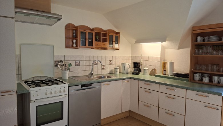 Küche, © Manuela Heher Eckküche mit Herd, Spüle, Geschirrspüler und Regalen.