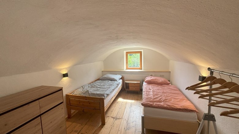 Doppelzimmer, © Michael Hofer Ein einfaches Doppelzimmer mit zwei Einzelbetten, einer Kommode und einem Kleiderständer. Ein kleines Fenster lässt Tageslicht herein.