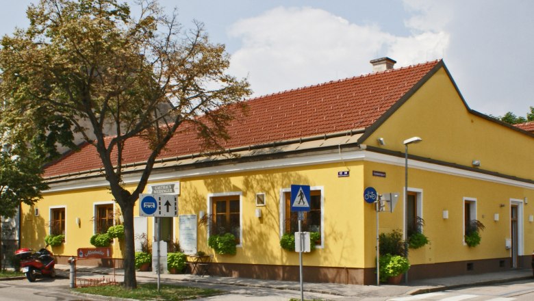 Weidinger Inn, © Wiener Alpen/Katrin Zeleny Yellow building with a red roof, signposted as Gasthaus Weidinger, on a street corner with crosswalk and traffic signs.