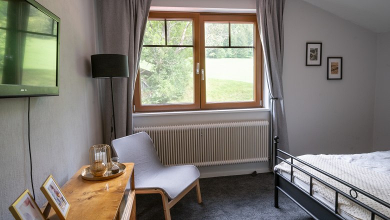 Schlafzimmer Ferienhaus Schlager Obergschoss, © Claudia Schlager Schlafzimmer mit grauem Teppich, Bett, Sessel, Fernseher und Fenster mit Blick ins Grüne.