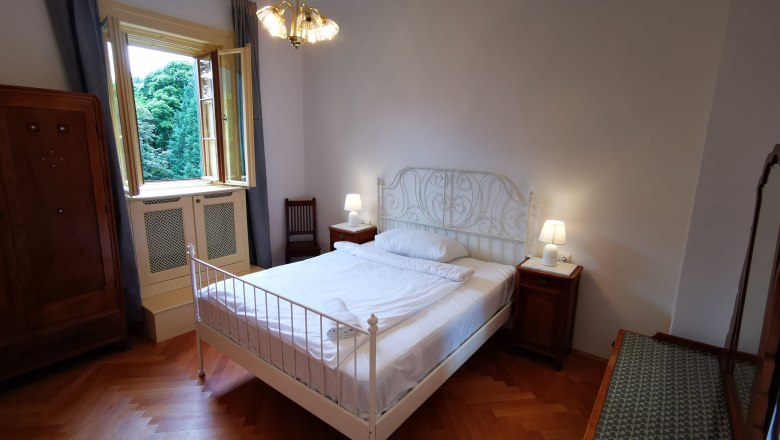 Schlafzimmer im Appartement Josef, © Herrnhof Schlafzimmer mit Doppelbett, Nachttischen und offenem Fenster mit Blick auf Bäume.