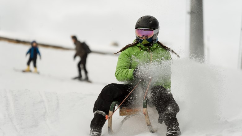 Tobogganing on the Semmering, © Semmering Hirschenkogel Person wearing a green anorak and helmet riding a sledge in the snow.