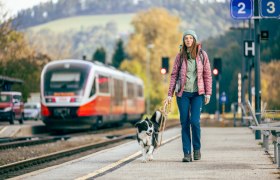 Bahnhof Aspang, © Wiener Alpen, Kremsl Frau mit Hund am Bahnhof Aspang, Zug im Hintergrund.