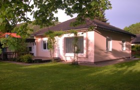 Ferienhaus Tauchner, © Johann Tauchner Ein rosa gestrichenes Ferienhaus mit dunklem Dach, umgeben von einem grünen Garten und Bäumen.