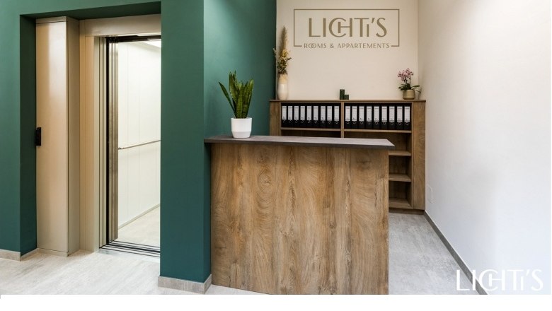 Empfangsbereich, © Lichti´s Appartements-Christian Kremsl Empfangsbereich mit Holztheke, grünem Wandbereich und Aufzug.