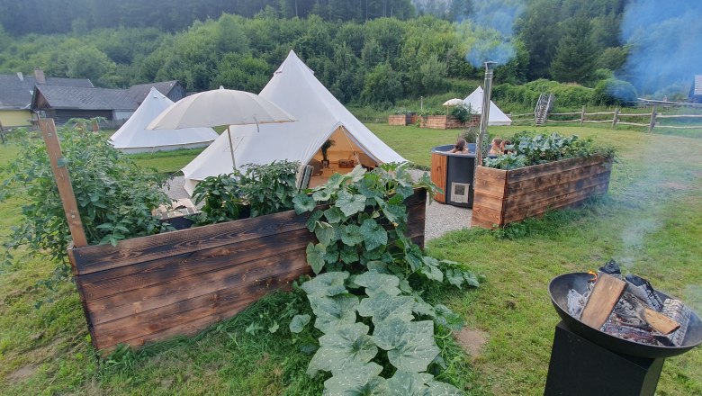 Glamping - Wildnis Zentrum Nasswald, © Jonathan Clark Glamping-Zeltplatz mit Feuerstelle und Hot Tub in grüner Umgebung.