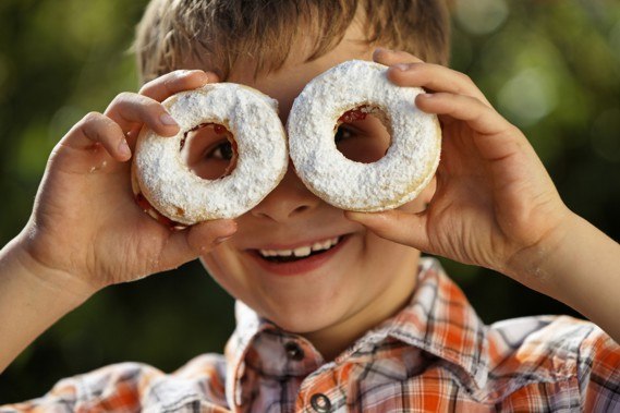 lucas, © SchaglOG A boy holds two doughnuts sprinkled with powdered sugar in front of his eyes.