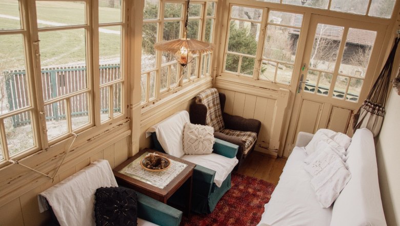 Orlet an der Rax, © Sofia Orlet Gemütlicher Wintergarten mit Sesseln, Sofa und Tisch, umgeben von großen Fenstern mit Blick ins Freie.