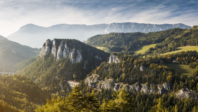 Semmeringbahn, © NÖW Michael Liebert Panoramablick auf die Semmeringbahn in einer bergigen Landschaft mit Wäldern und einem Viadukt.