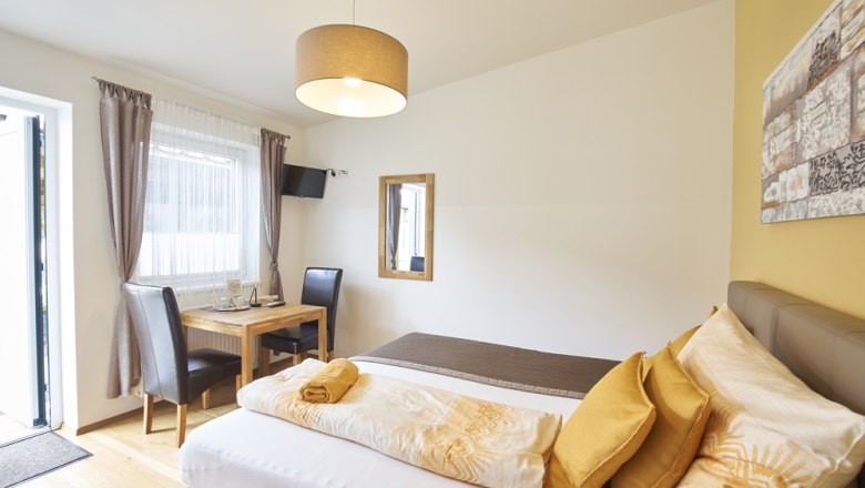 Zimmer Riesling, Gästezimmer Victoria, © Marianne Graf Helles Gästezimmer mit Bett, Tisch, Stühlen und Fernseher.