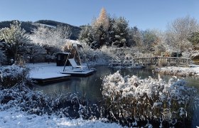 Paradiesgart' im Winter, © Hotel Molzbachhof, Peter Pichler Winterlicher Garten mit Teich, Brücke und Schaukel im Schnee.