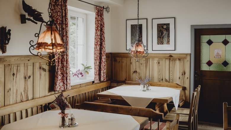 Rastplatz nach Wandertour oder Skivergnügen, © Niederösterreich-Werbung/Sophie Menegaldo Gemütlicher Gastraum mit Holzmöbeln, roten Vorhängen und dekorativen Lampen.