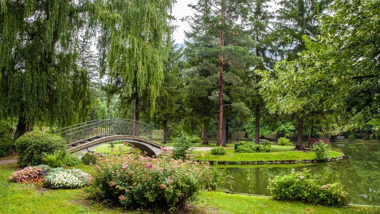 Kurpark Reichenau, © Wiener Alpen/Nadja Meister Ein idyllischer Park mit einer kleinen Brücke über einen Teich, umgeben von Bäumen und Blumen