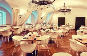 Wappensaal im das Freiherr, © Markus Jokesz Eleganter Speisesaal mit Parkettboden, weißen Stühlen, Holztischen und dekorativen Kronleuchtern.