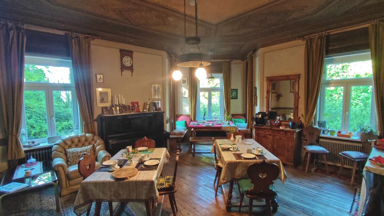 Frühstückssalon, © Villa Petterhof Ein gemütlicher Frühstückssalon mit gedeckten Tischen, antiken Möbeln und großen Fenstern, die viel Tageslicht hereinlassen.