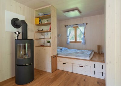 Huberto modular house, © Carina Rebler Interior view of a modular house with wood stove, shelf and bed.