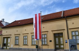 Außenansicht Städtisches Museum Neunkirchen, © Vanessa Staundenhirz Außenansicht des Museums Neunkirchen mit österreichischer Flagge und Informationsschild.
