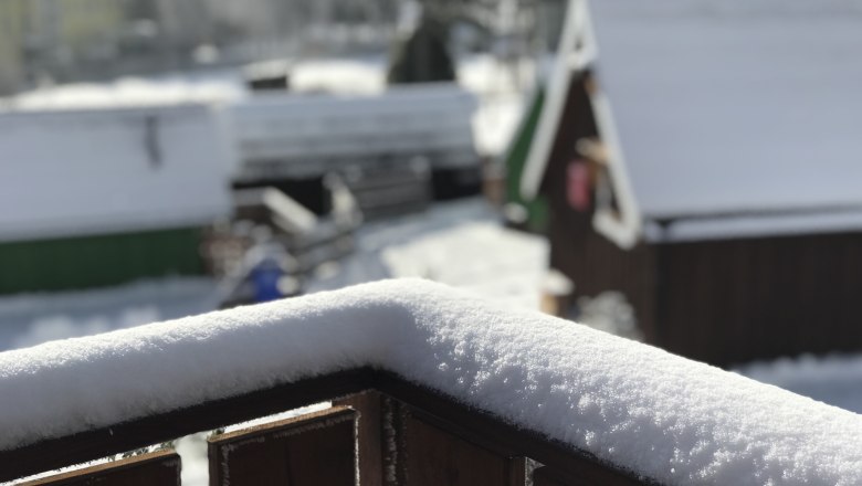 Glamping Park im Winter, © Glamping-Park Mönichkirchen OG Verschneite Holzbalken im Vordergrund, unscharfe Hütten im Hintergrund.