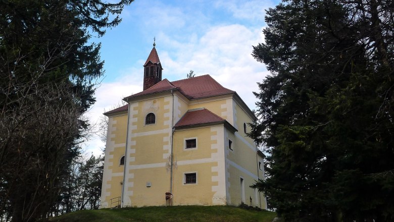 Rosalienkapelle, © alpenlandmagazin.at Kapelle mit gelber Fassade auf einem Hügel, umgeben von Bäumen.