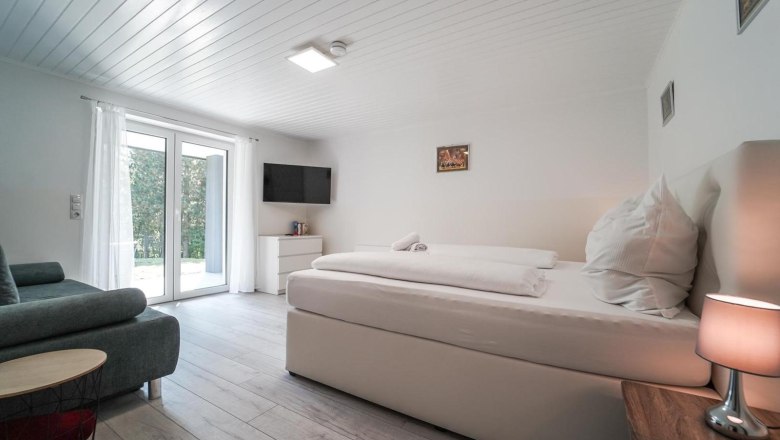Schlafzimmer, © Michaela Narath Modernes Schlafzimmer mit großem Bett, Sofa, Fernseher und Glastür.