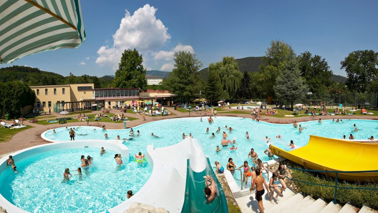 Naturbad Gloggnitz, © Wiener Alpen, Foto: Franz Zwickl Ein Freibad mit mehreren Pools, Wasserrutschen und vielen Menschen an einem sonnigen Tag.