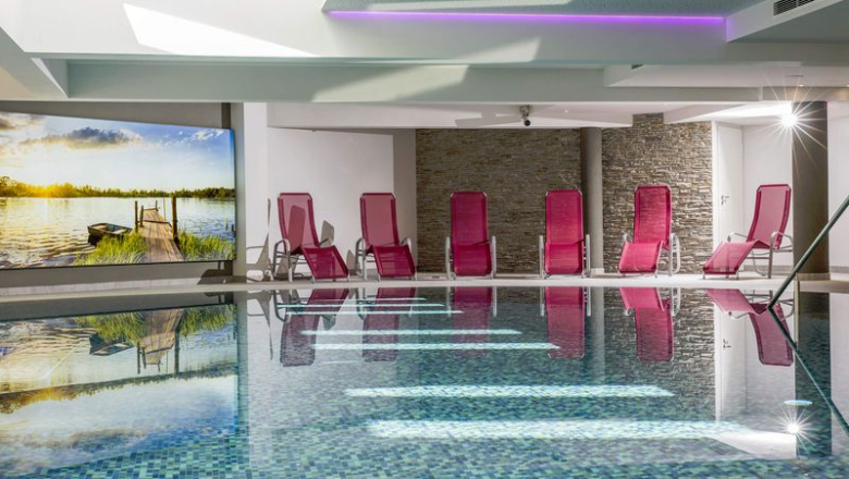 Hallenbad, © Vivea Gesundheitshotel Hallenbad mit roten Liegestühlen, Steinwänden und einem großen Wandbild.