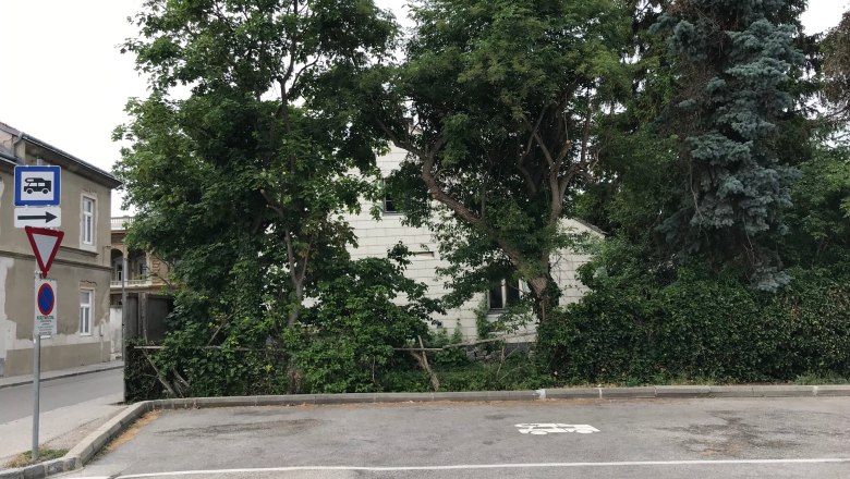 Camping pitch, © Birgit Rada-Tomasin An empty parking lot with a motorhome symbol on the ground, surrounded by trees and a building in the background.
