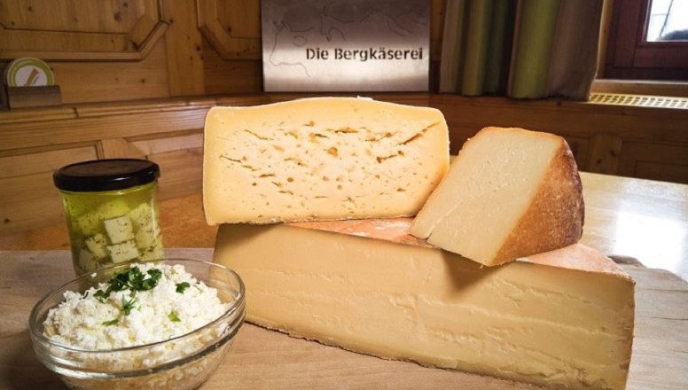 Hochwertige Produkte aus reinsten Rohstoffen, © Familie Ungersböck Verschiedene Käsesorten auf einem Holzbrett mit einem Glas eingelegtem Käse und einer Schüssel Frischkäse.