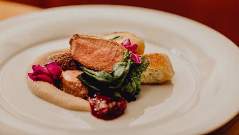 Pink roast duck with cream tartlets & chestnut purée, © Niederösterreich Werbung/Klaus Engelmayer A plate of pink roast duck, cream tartlets, chestnut purée and green leaves, garnished with edible flowers.