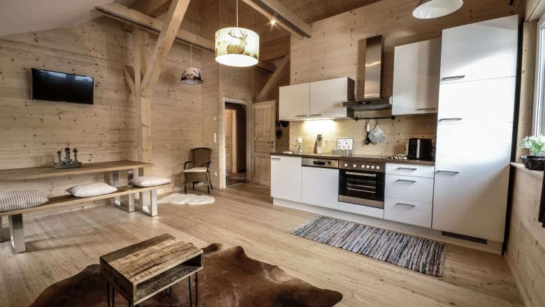 Steirer Apartment, © Stefan Zimprich Gemütliches Apartment mit Holzwänden, moderner Küche, Esstisch und Fernseher. Rustikaler Stil mit Teppich und Holzmöbeln.
