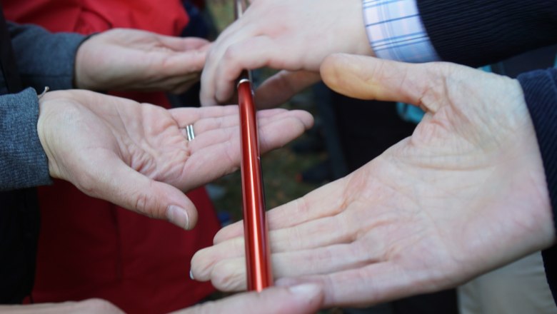 Teamwandern Incentives, © Wolfgang Menzel Menschen halten gemeinsam einen roten Stab mit den Fingern.