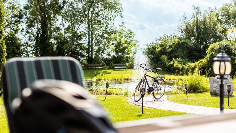 Garten, © Wiener Alpen / Martin Fülöp Ein Fahrrad steht neben einem Teich mit Springbrunnen in einem sonnigen Garten.