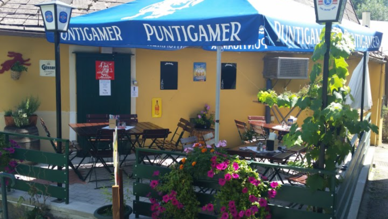 Stiegenwirtshaus Gloggnitz, © Stiegenwirtshaus/Stummer Außenbereich eines Wirtshauses mit blauen Sonnenschirmen und Blumen.