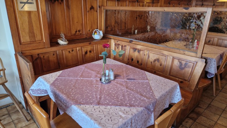 Gastzimmer, © Karin Stranz Ein gemütlicher Tisch in einem rustikalen Gastzimmer mit Holzvertäfelung, Tischdecke und einer Vase mit Blume.