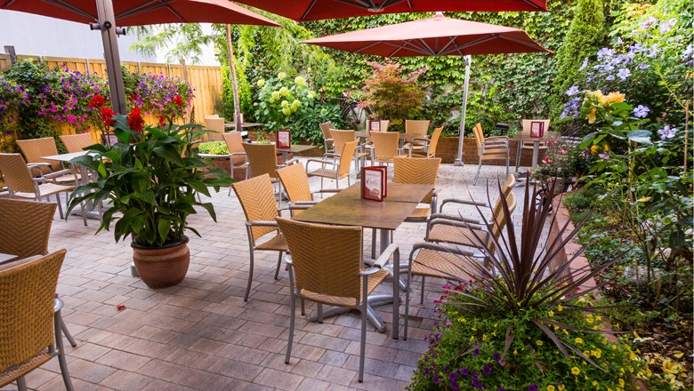 Bistro with guest garden, © Koll GmbH A cozy guest garden with tables, chairs and parasols, surrounded by lush plants.