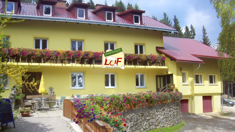 Gasthaus Luf, © Gasthaus Luf, Foto Uno GmbH Gelbes Gasthaus mit roten Dächern und blühenden Blumen auf dem Balkon.