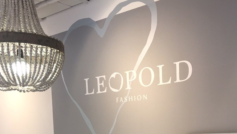 Café Leopold, © Sandra Jurasovits Ein Kronleuchter hängt vor einer grauen Wand mit der Aufschrift 'LEOPOLD FASHION' und einem Herzmotiv.