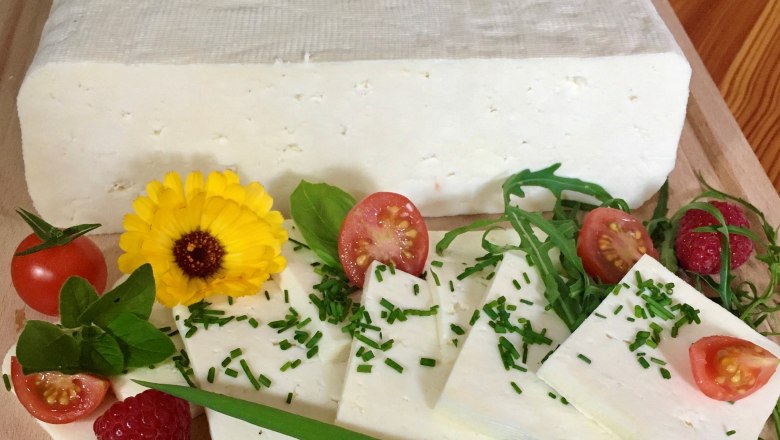 Sheep's cheese from the Kölbel organic sheep farm, © Kölbel A block of sliced sheep's cheese, garnished with tomatoes, raspberries, rocket and a yellow flower on a wooden board.