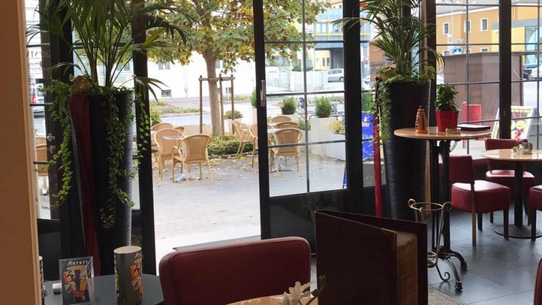 Café Stadler beim Bahnhof, © Café Stadler Innenansicht eines Cafés mit Blick auf eine Terrasse mit Tischen und Stühlen.