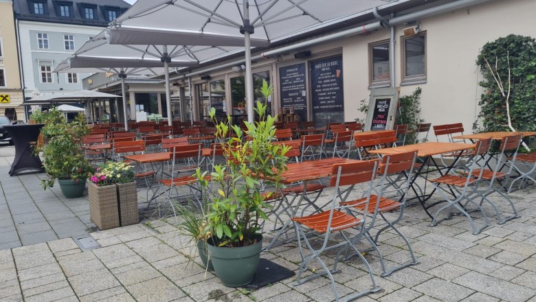 Siegl's Pub, © Siegl's Pub Außenbereich eines Pubs mit leeren Holztischen und -stühlen unter großen Sonnenschirmen.