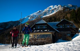 Edelweisshütte Schneeberg, © Wiener Alpen, Claudia Ziegler Zwei Skifahrer vor der Edelweisshütte am Schneeberg mit schneebedecktem Berg im Hintergrund.