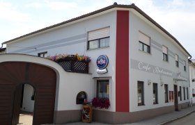 Café Restaurant Sabine, © Sabine Schneeweis Außenansicht Café Sabine mit Holztor, weiß-roter Fassade und Aufschrift "Café-Restaurant".