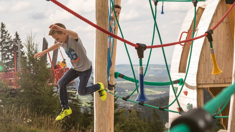 Kletterspaß am Abenteuer-Spielplatz, © Erlebnisalm Mönichkirchen, Martin Fülöp Kinder spielen auf einem Klettergerüst im Freien.