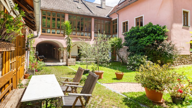 Innenhof - Ferienwohnungen Manuela, © Wiener Alpen / Christian Kremsl Innenhof mit Gartenmöbeln, Pflanzen und rosa Gebäude im Hintergrund.