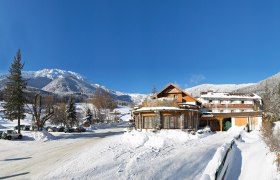 Forellenhof, © Forellenhof, Martin Wanzenböck Winterlandschaft mit Hotel Forellenhof vor schneebedeckten Bergen und blauem Himmel.