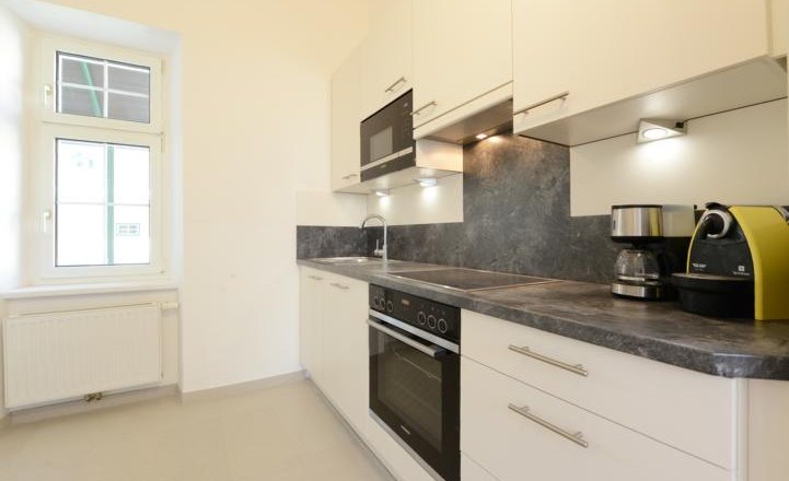 Apartment G1 in the Gerhardthof Reichenau, © Gerhardthof Reichenau Modern kitchen with white cupboards, gray worktop, oven, microwave and coffee machines.